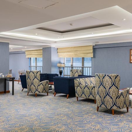 Al Aqeeq Madinah Hotel Медина Экстерьер фото The photo shows a stylish indoor lounge or sitting area. It features several upholstered armchairs arranged around a central space. The chairs have a blue and cream patterned upholstery, creating a sophisticated ambiance. There is a table alongside s
