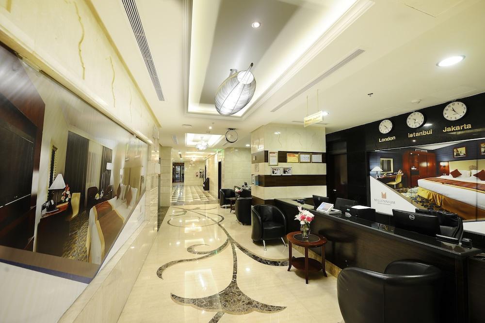 Al Aqeeq Madinah Hotel Медина Экстерьер фото The photo shows the interior of a hotel lobby or reception area. It features a sleek, modern design with elegant marble flooring, decorative lighting fixtures on the ceiling, and a sophisticated color scheme. There are comfortable black seating areas