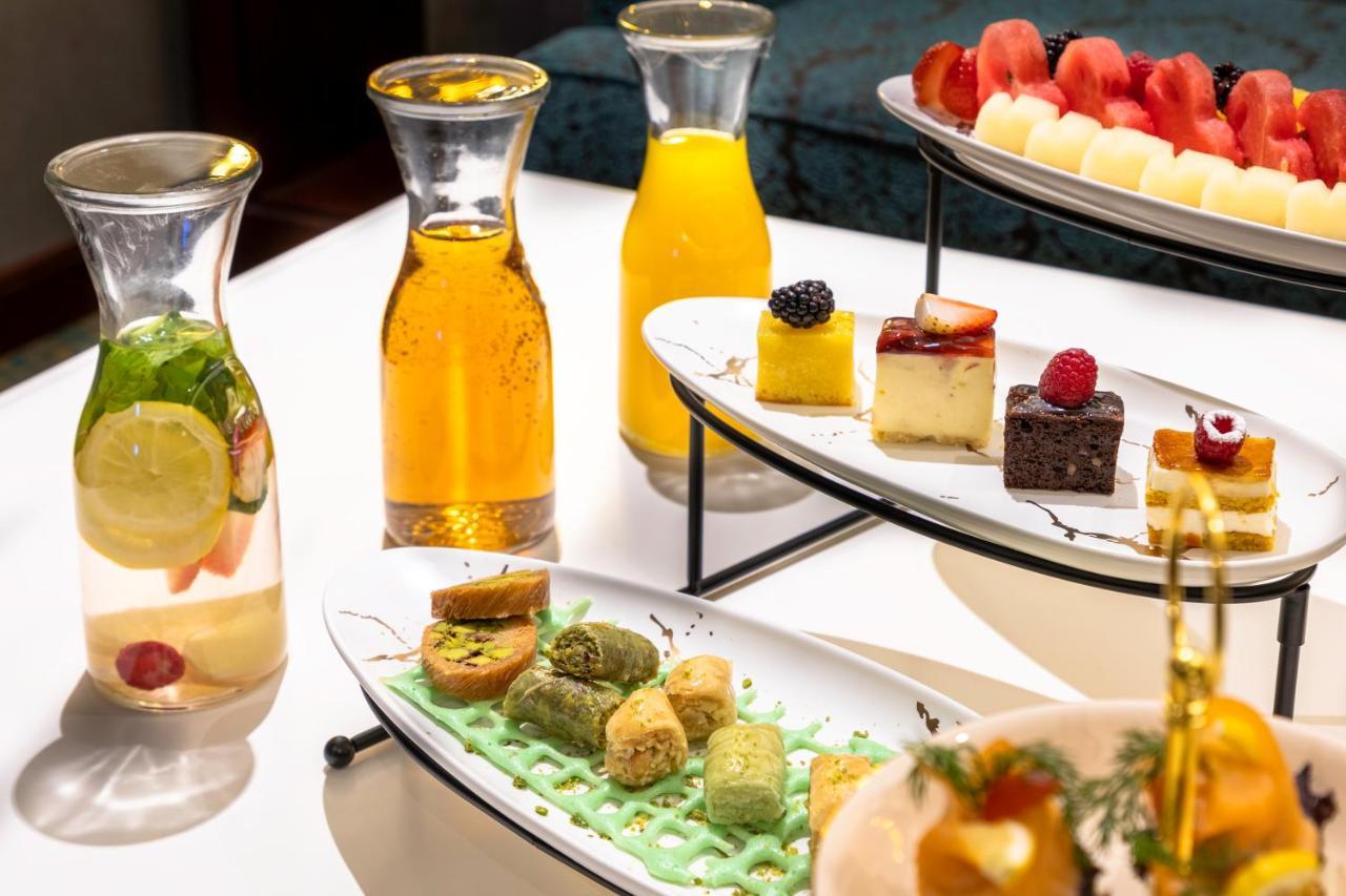 Al Aqeeq Madinah Hotel Медина Экстерьер фото The photo showcases an elegant display of refreshments and desserts. There are several glass pitchers filled with bright, colorful beverages, likely juices or infused water, one featuring lemon and mint. A two-tier serving stand holds an assortment o