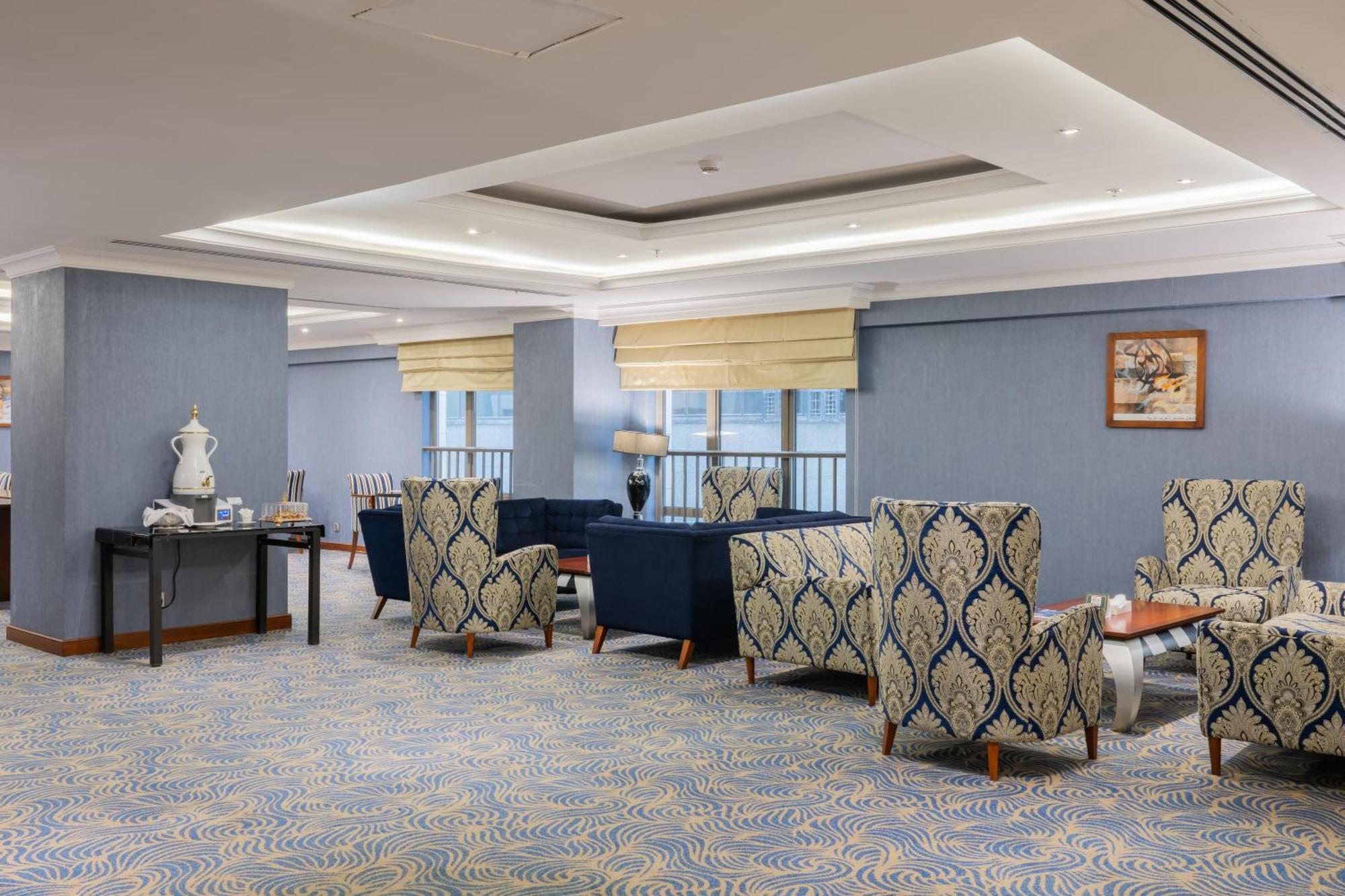 Al Aqeeq Madinah Hotel Медина Экстерьер фото The photo shows a stylish indoor lounge or sitting area. It features several upholstered armchairs arranged around a central space. The chairs have a blue and cream patterned upholstery, creating a sophisticated ambiance. There is a table alongside s