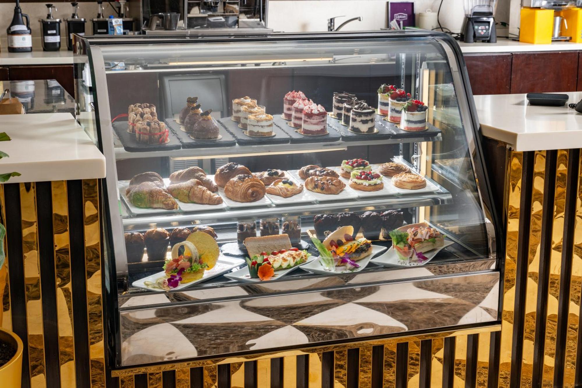 Al Aqeeq Madinah Hotel Медина Экстерьер фото The photo shows a display case filled with an assortment of desserts. There are various types of pastries, including cakes, tarts, and croissants, arranged neatly on different shelves. The desserts are visually appealing, with colorful decorations, f