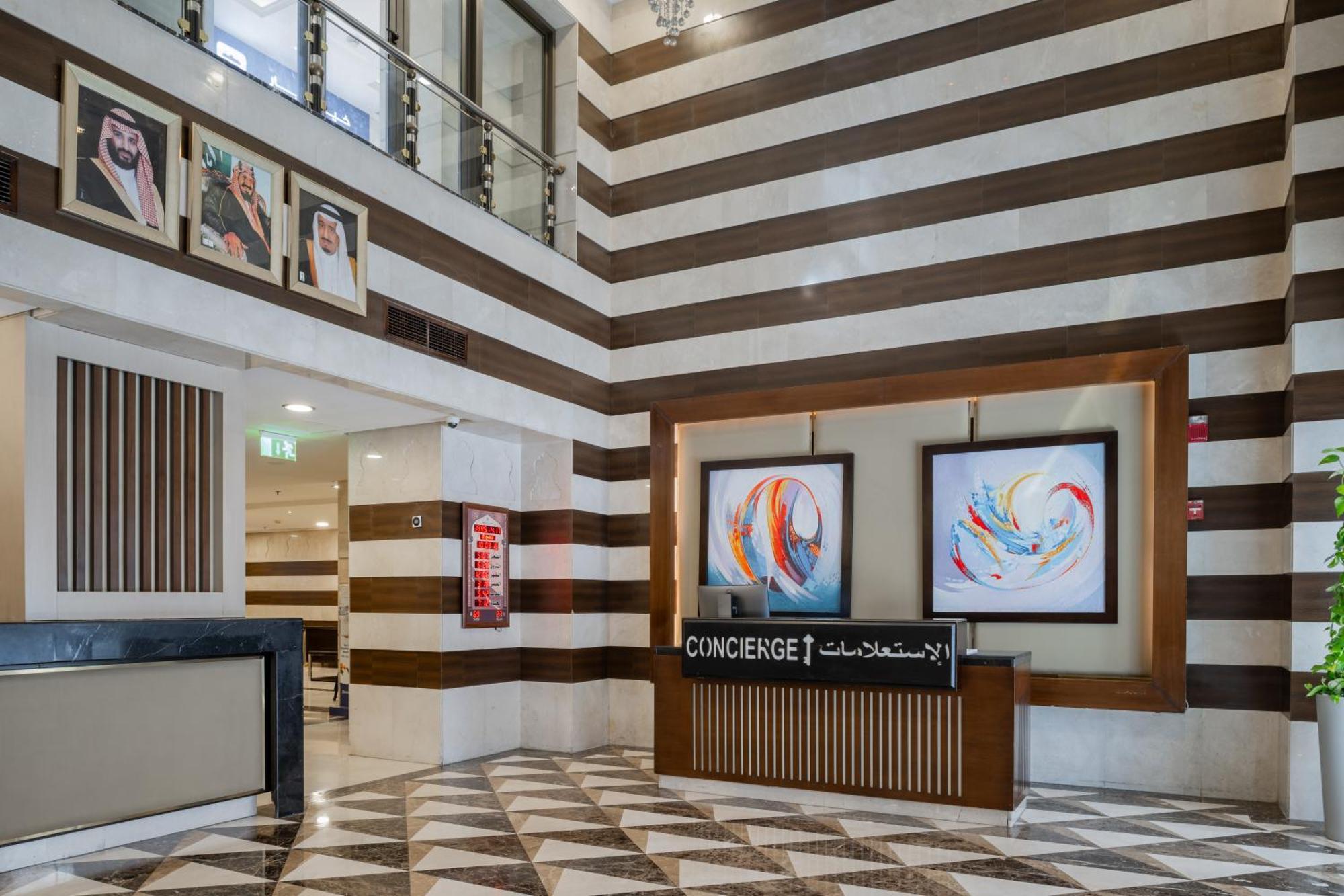 Al Aqeeq Madinah Hotel Медина Экстерьер фото The photo shows a modern hotel lobby area characterized by its stylish design. The walls feature a pattern of horizontal stripes in different shades, creating a sophisticated atmosphere. To the left, there is a reception area with a sleek desk labele