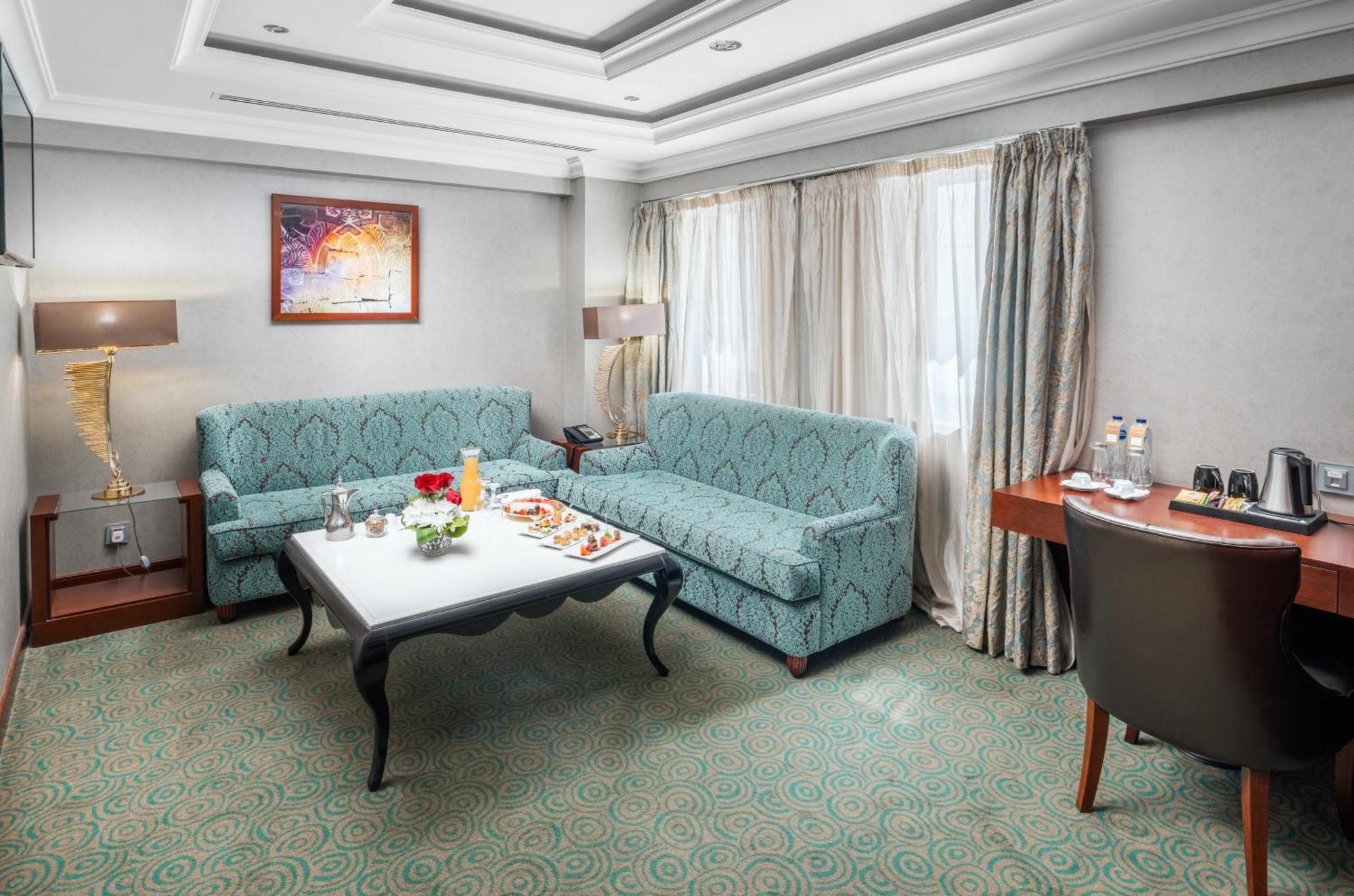 Al Aqeeq Madinah Hotel Медина Экстерьер фото The photo shows a cozy hotel room or lounge area. It features two light blue sofas arranged around a low coffee table. On the table, there are snacks or refreshments arranged aesthetically. The room has a neutral color palette with a textured carpet 