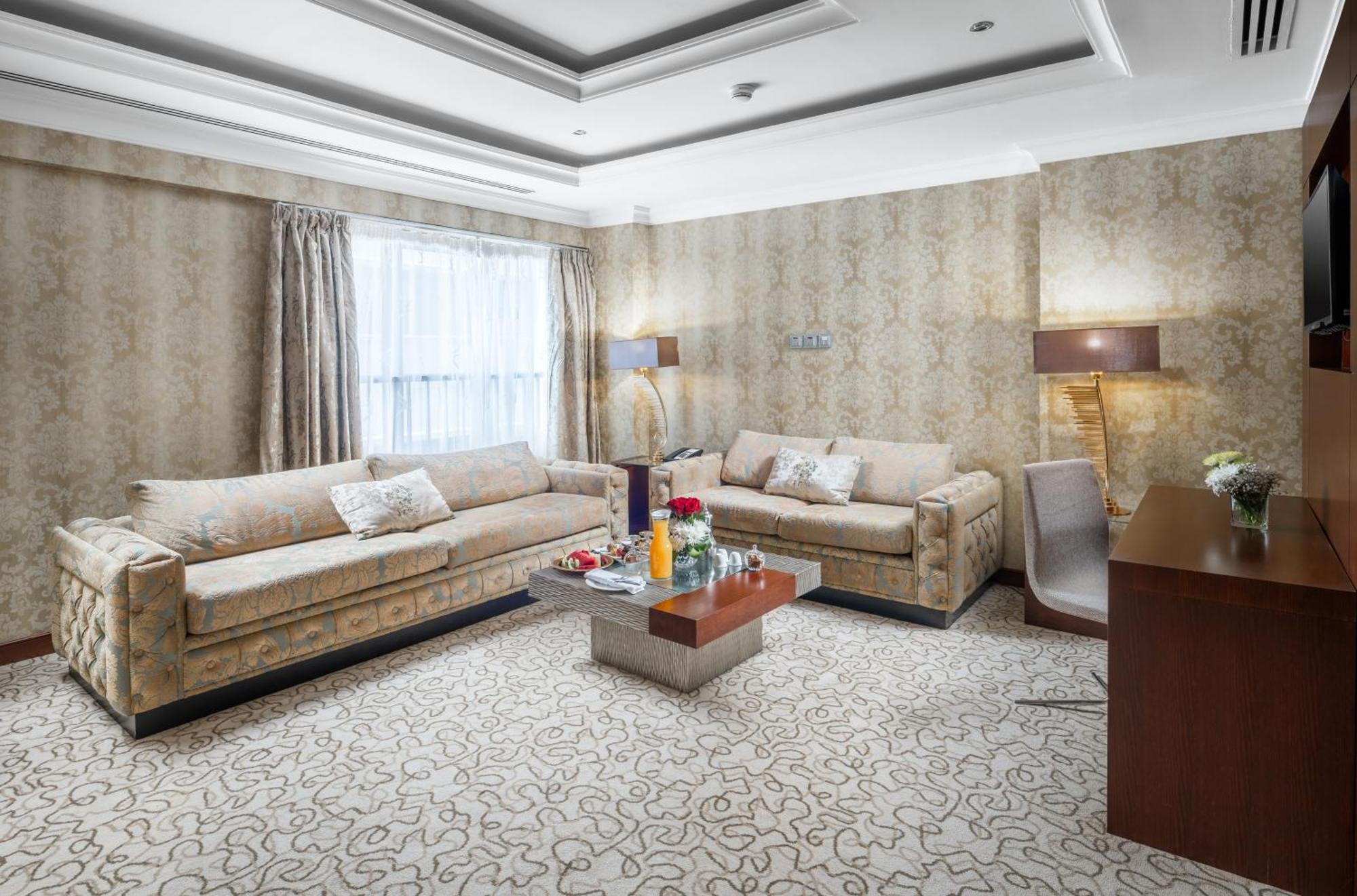 Al Aqeeq Madinah Hotel Медина Экстерьер фото The photo shows a stylish living room with an elegant design. There are two beige sofas placed opposite each other, adorned with decorative pillows. A low coffee table is positioned in the center, featuring various items, possibly drinks or decorativ