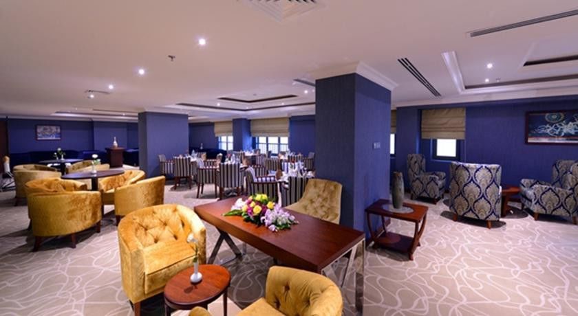 Al Aqeeq Madinah Hotel Медина Экстерьер фото The photo shows a stylish interior of a restaurant or dining area. It features elegantly arranged seating with plush, gold-colored chairs and a wooden table at the center, adorned with a floral arrangement. The background includes more dining tables,