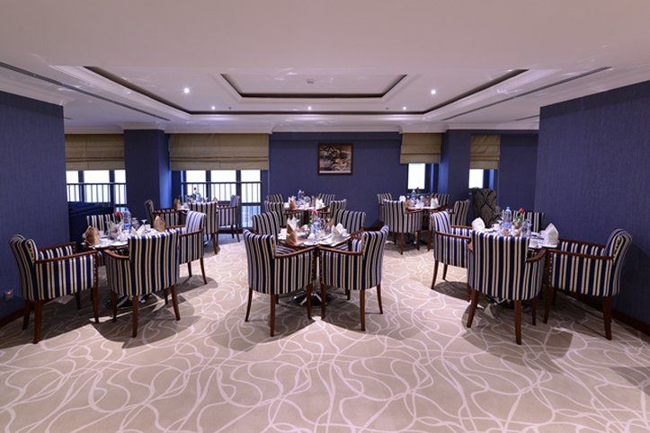 Al Aqeeq Madinah Hotel Медина Экстерьер фото The photo shows an elegant dining room equipped with several tables. Each table is set with white tableware and neatly arranged silverware, giving a formal dining appearance. The decor features striped chairs and a carpet with a subtle pattern. The w