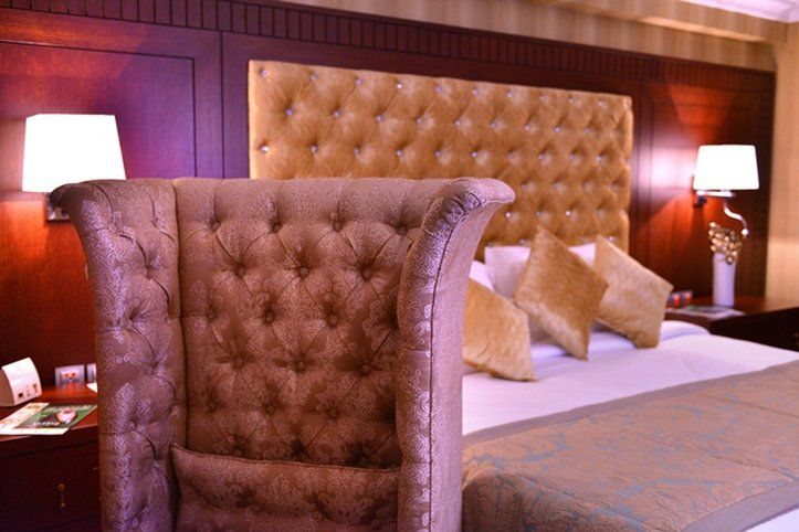 Al Aqeeq Madinah Hotel Медина Экстерьер фото The image shows a luxurious bedroom featuring a large upholstered headboard with a tufted design in a soft, beige color. The bed is elegantly dressed with decorative pillows and a textured bedspread. In the background, there are wooden paneling and s