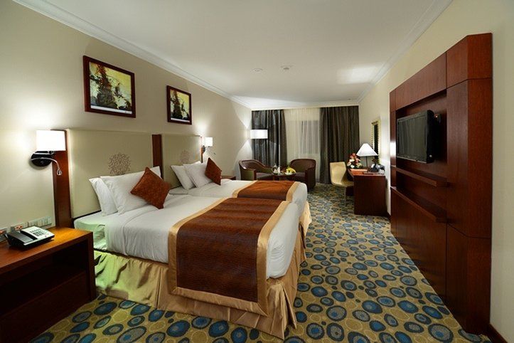 Al Aqeeq Madinah Hotel Медина Экстерьер фото The photo shows a hotel room featuring two beds with white linens and brown throw blankets. There are decorative pillows on the beds. The room has a modern design, with wooden furniture including bedside tables and a large wooden unit that houses a t